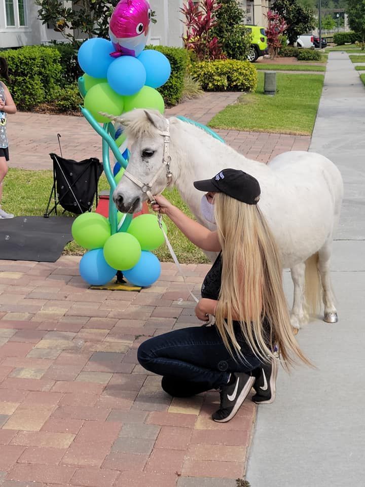 A woman kneeling down next to a pony with balloons in the background