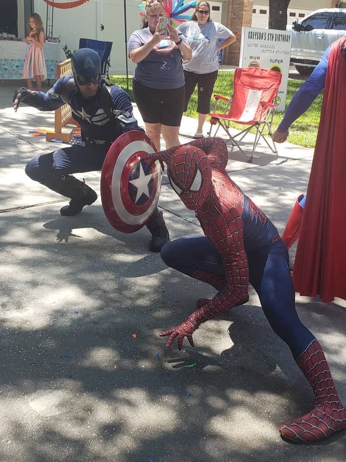 A man dressed as captain america is kneeling next to a man dressed as spiderman.