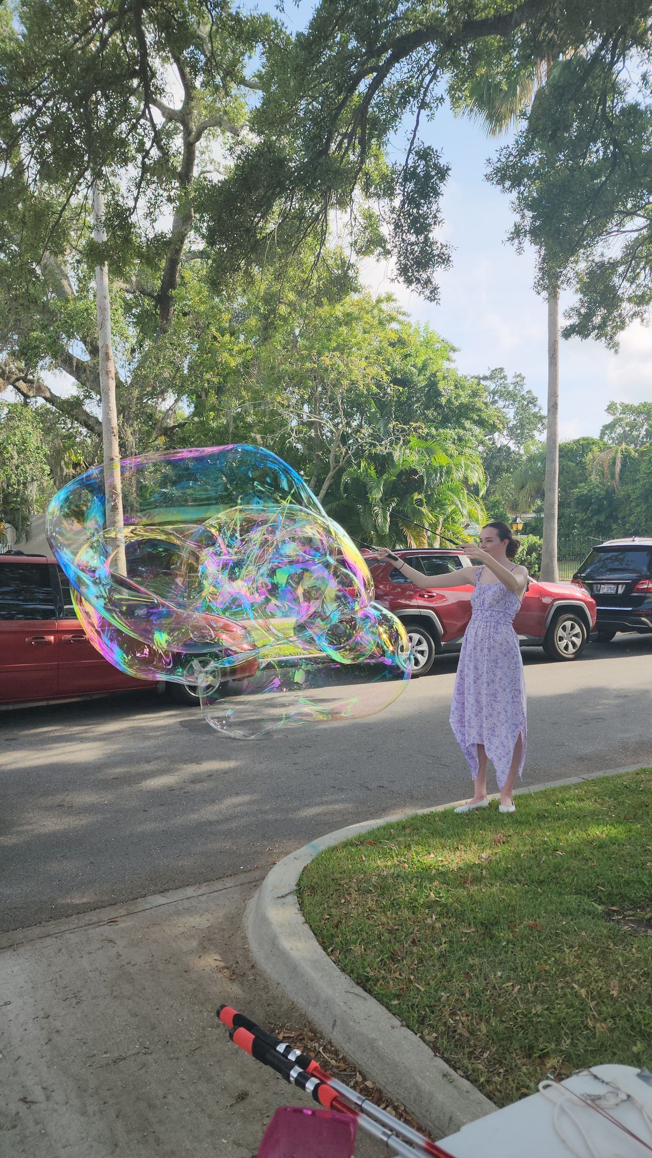 A woman is blowing a giant soap bubble in a parking lot.
