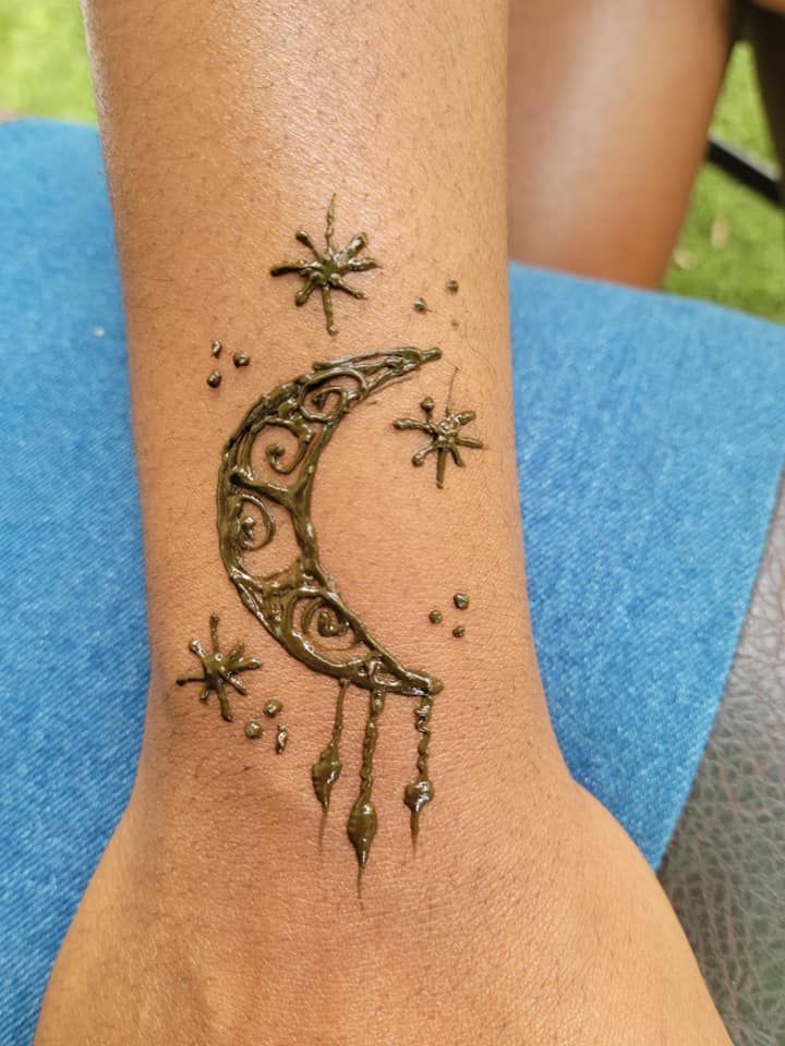A person has a tattoo of a crescent moon and stars on their wrist.