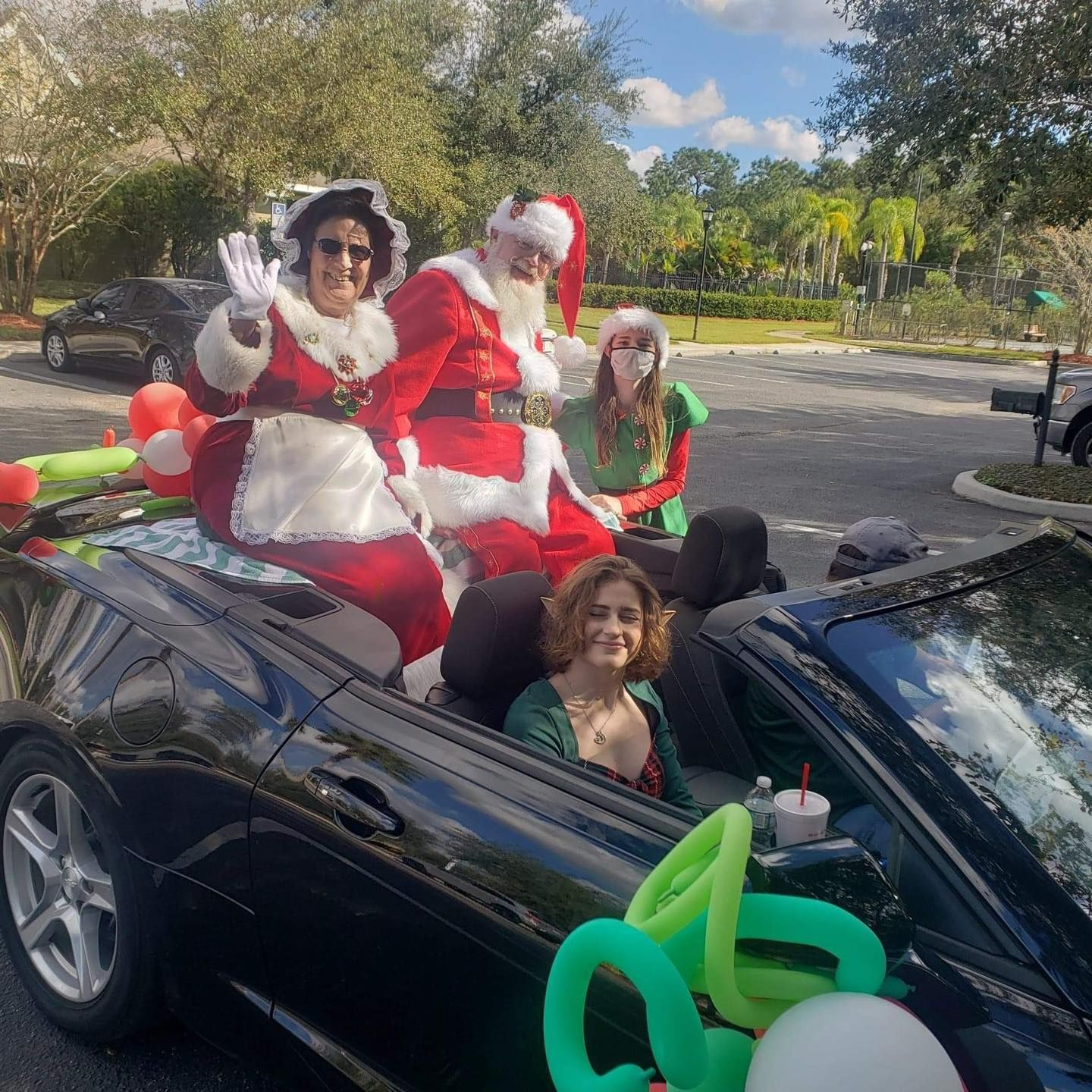 A group of people dressed as santa claus are riding in a convertible car.