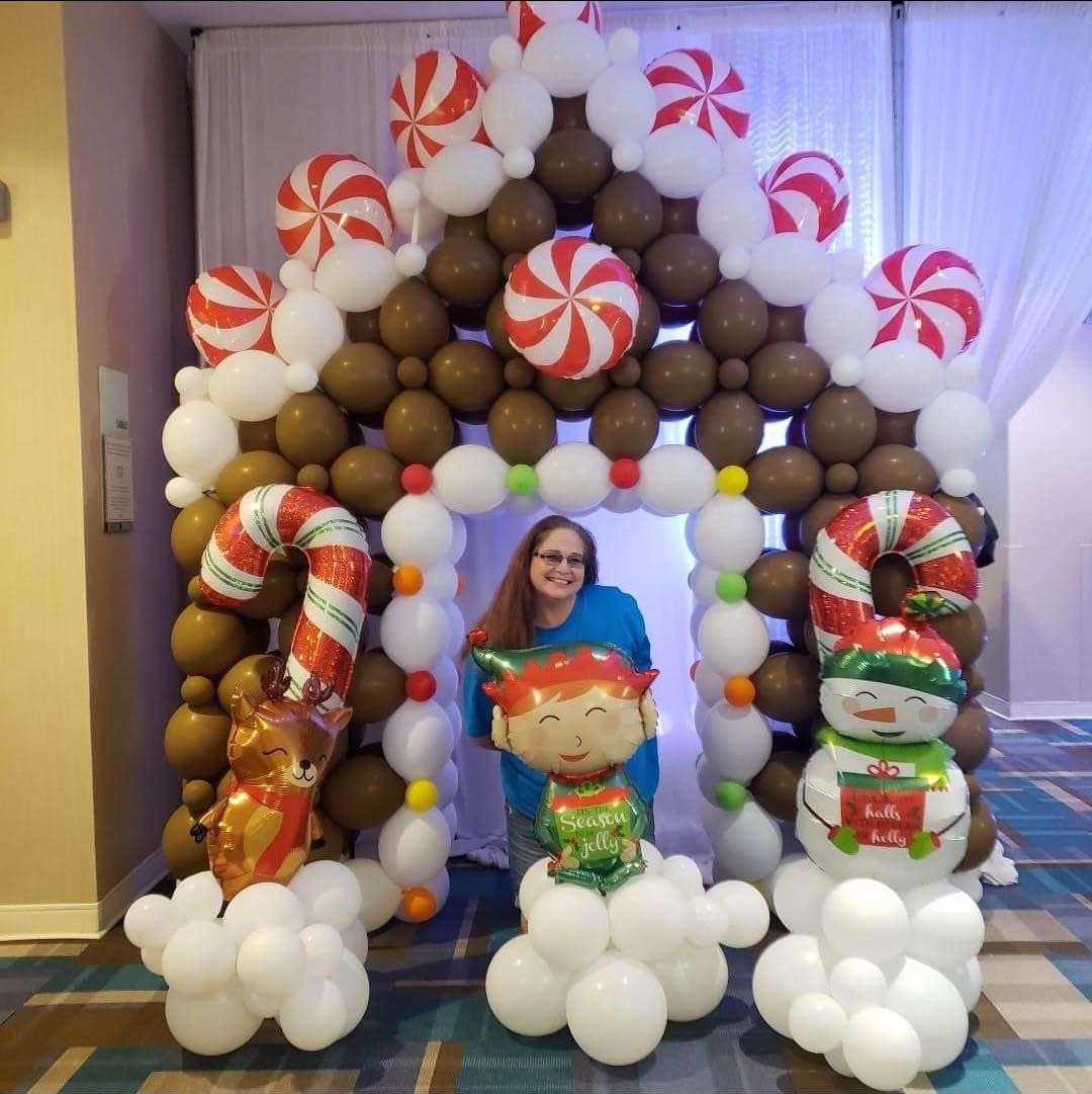 A woman is standing in front of a gingerbread house made of balloons