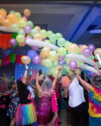 a group of people are dancing under a bunch of balloons
