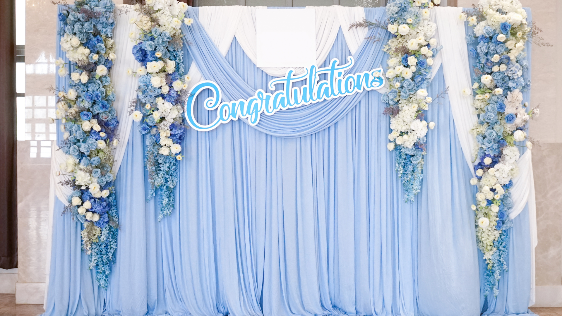 A blue and white backdrop with flowers and a sign that says `` congratulations ''.