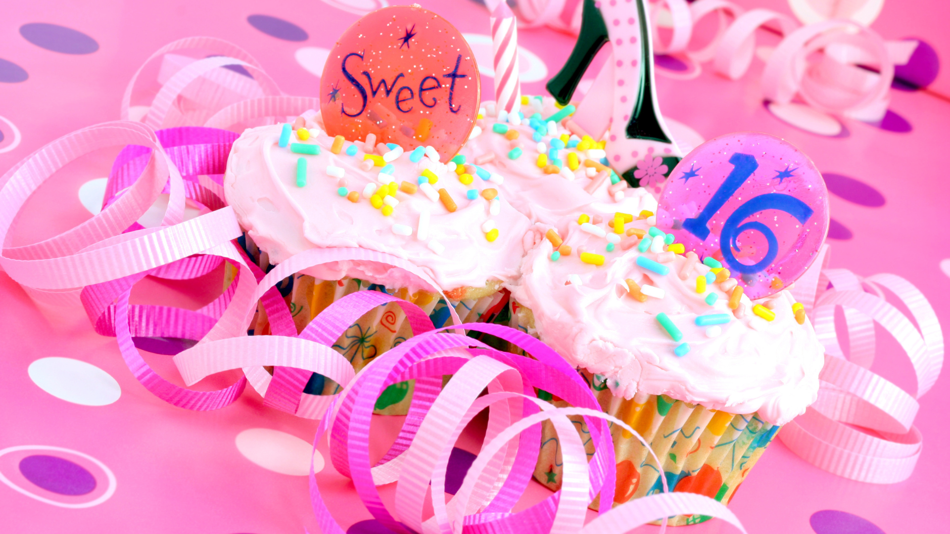 Two cupcakes with the number 16 on them are on a pink table.