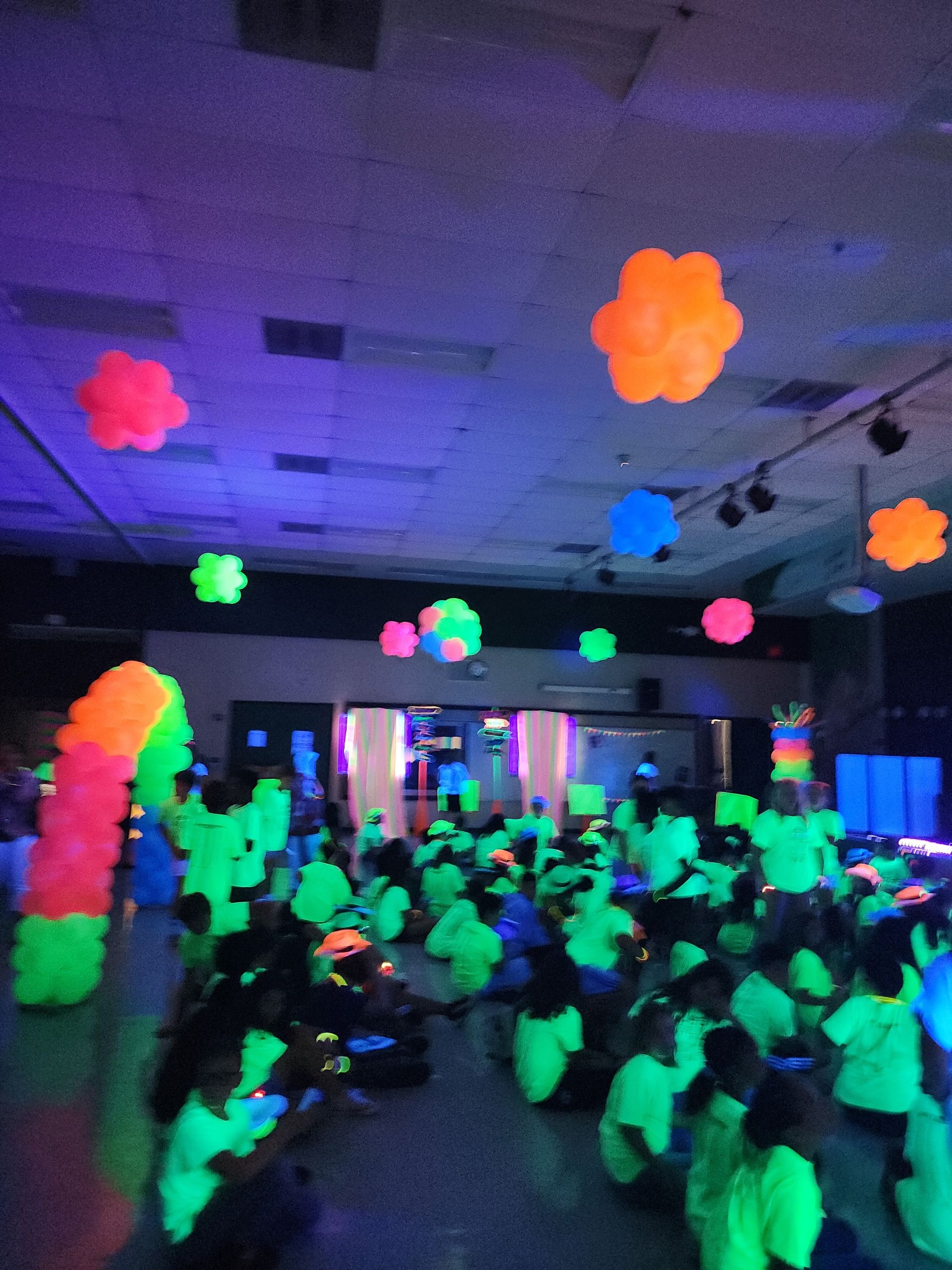 A group of people are sitting in a dark room with glow in the dark balloons hanging from the ceiling