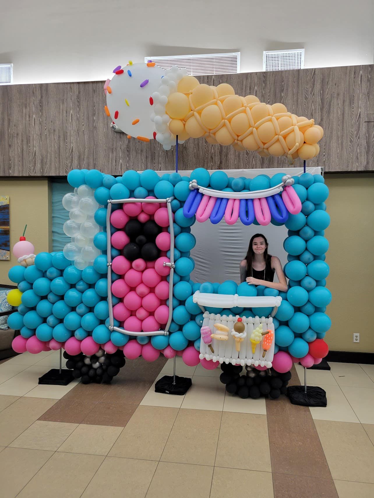 A woman stands in front of an ice cream truck made of balloons