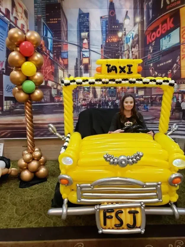 A woman is sitting in a taxi made out of balloons