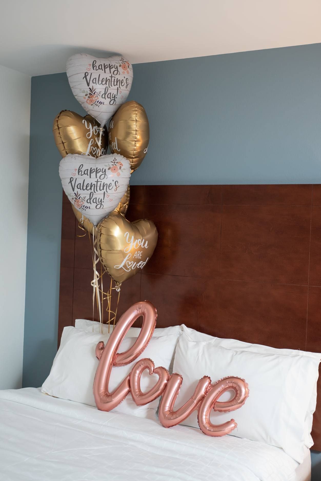 A bed with a bunch of balloons on it and a sign that says `` love ''.