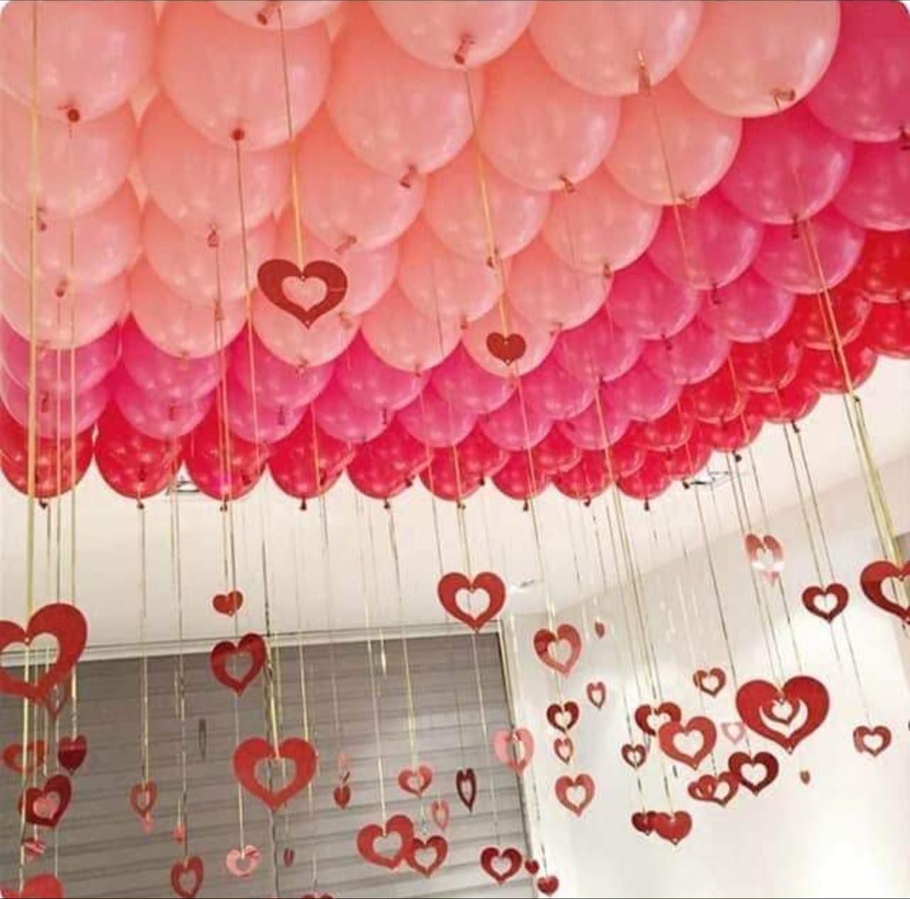 A bunch of pink and red balloons with hearts hanging from the ceiling