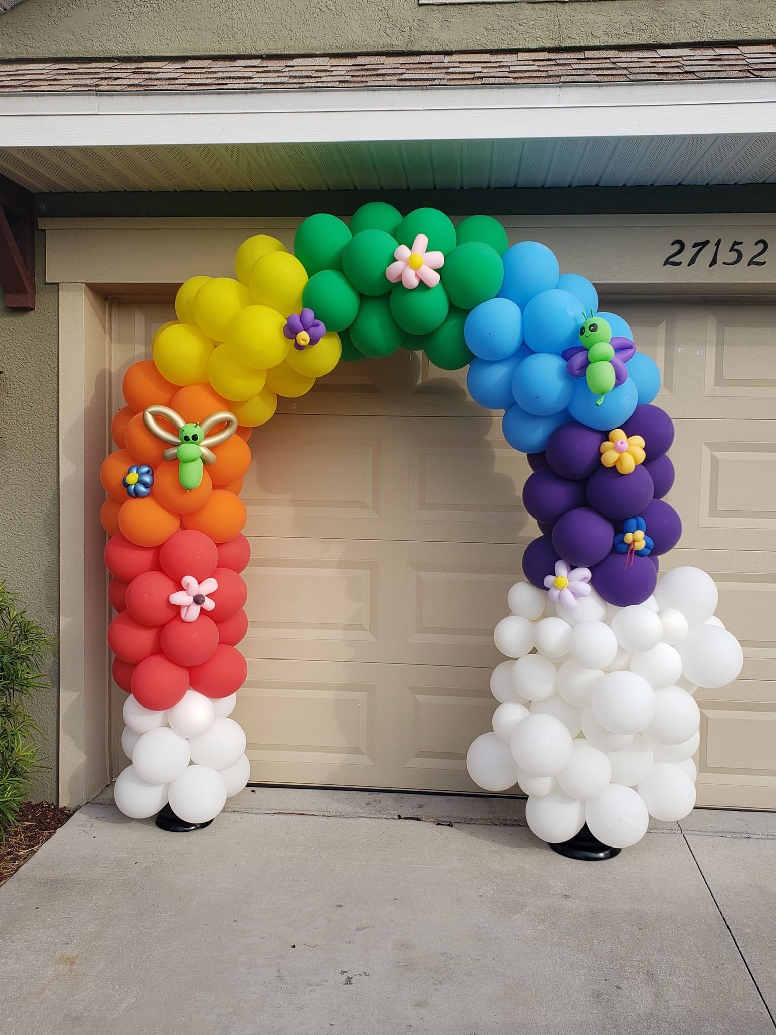 A rainbow colored balloon arch is sitting in front of a garage door.