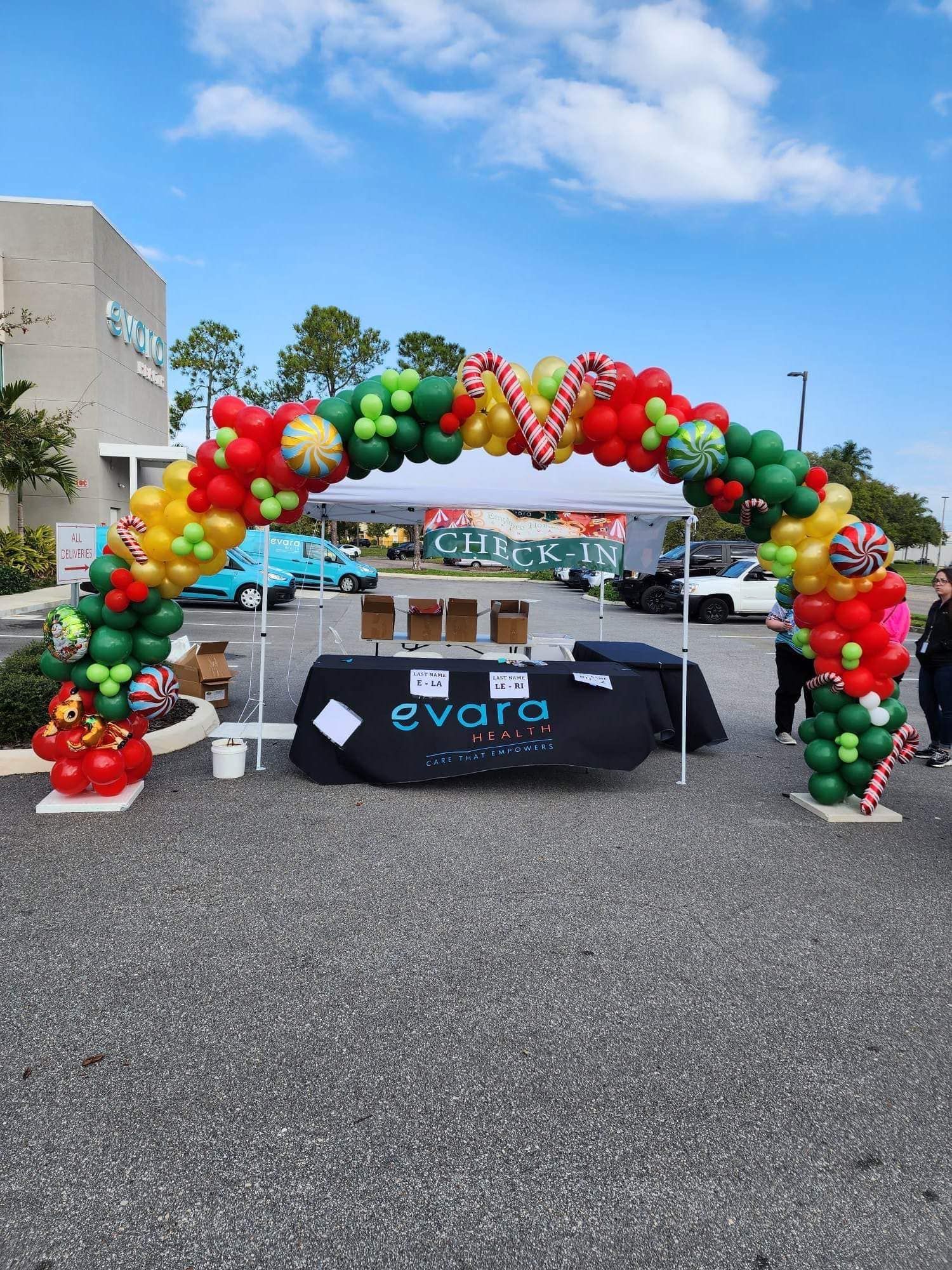 A table is sitting under a balloon arch in a parking lot.