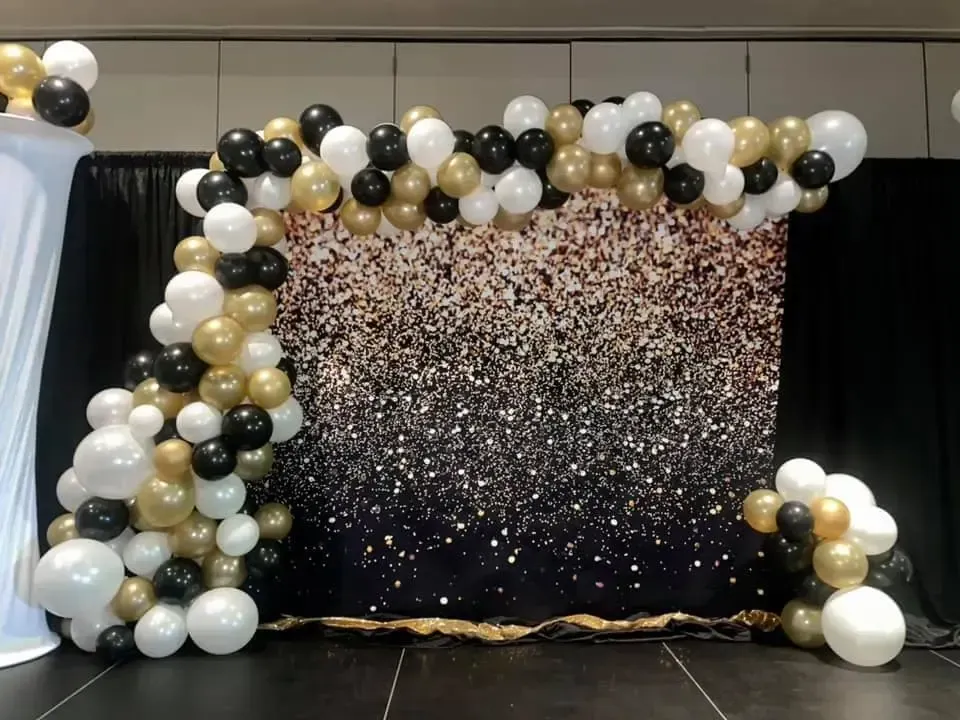 A wall covered in black , white , and gold balloons.