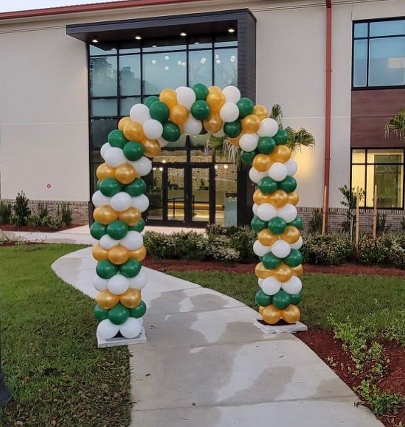 A green and gold balloon arch in front of a building