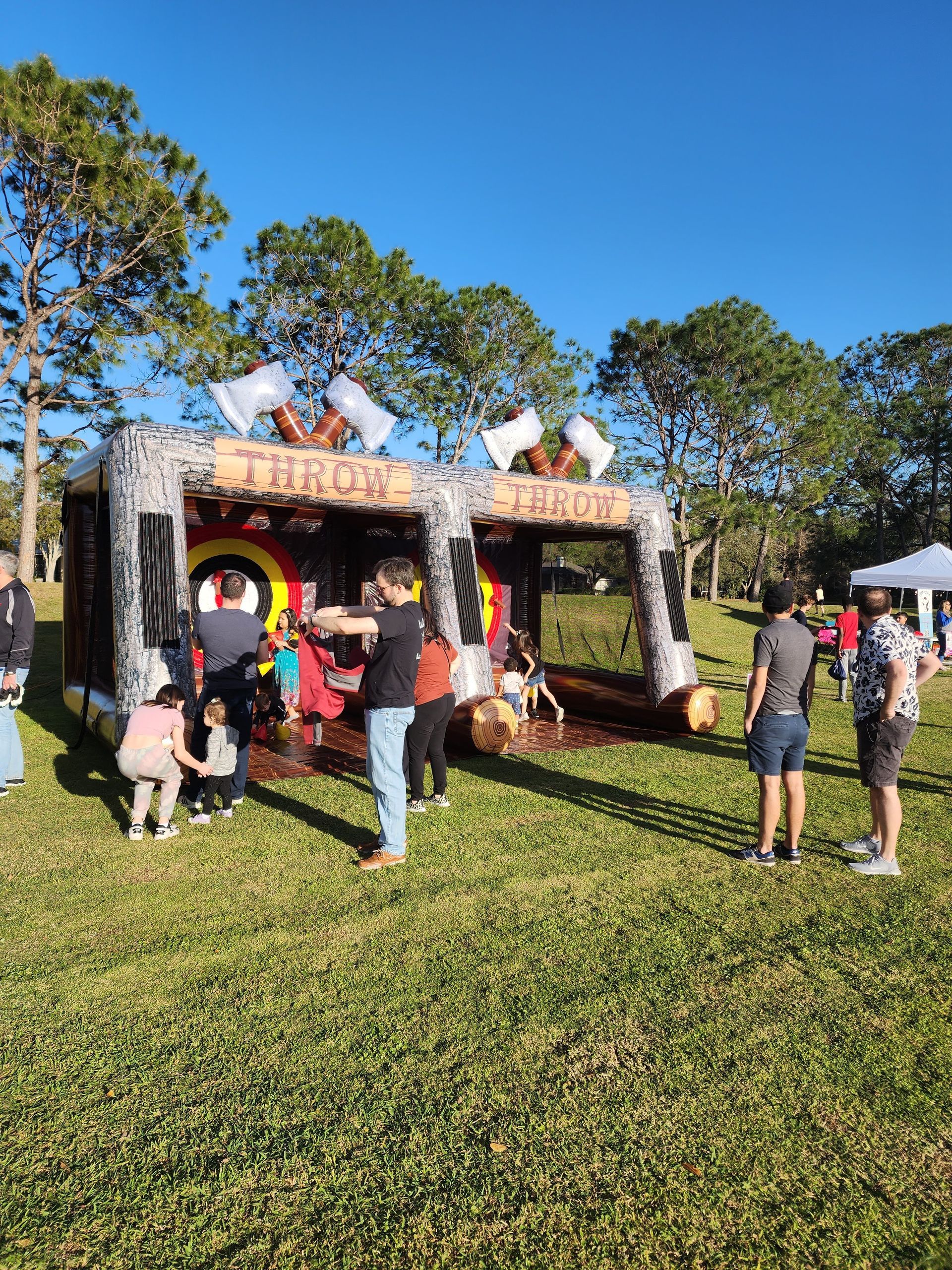 A group of people are standing in front of a bouncy house in a park.