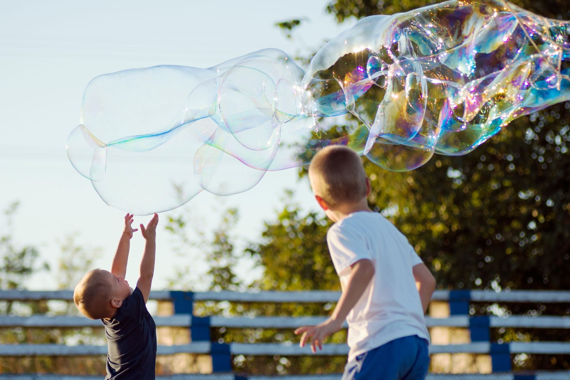 Two young boys are playing with soap bubbles in a park.