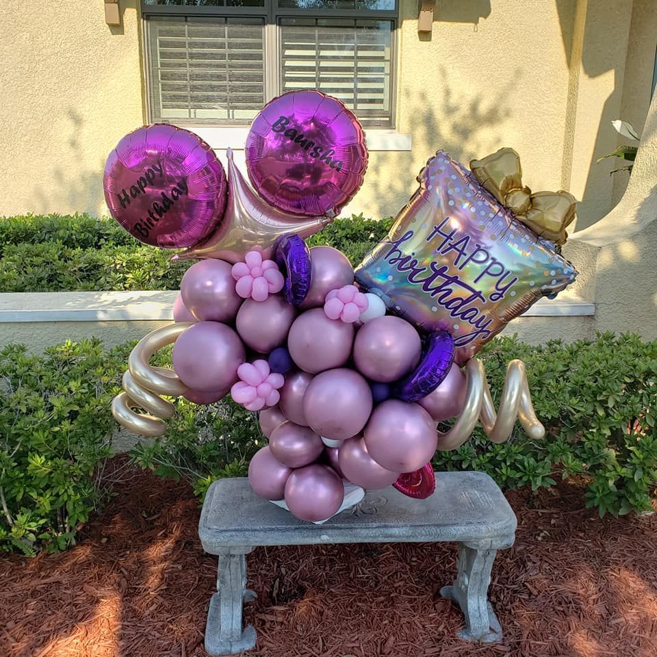 A bunch of pink and purple balloons are sitting on a bench.