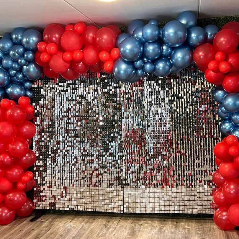 A wall covered in red , blue and silver balloons.