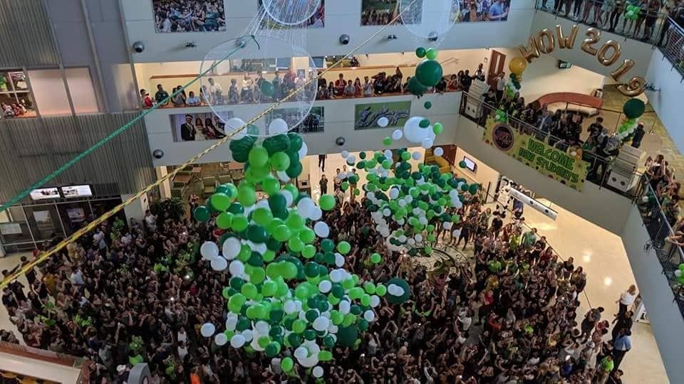 A large crowd of people are gathered in a mall with green and white balloons
