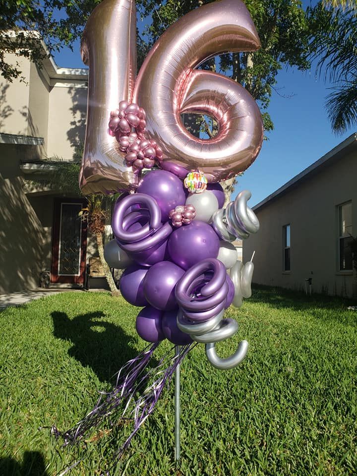 A bunch of balloons are sitting on top of a lawn in front of a house.