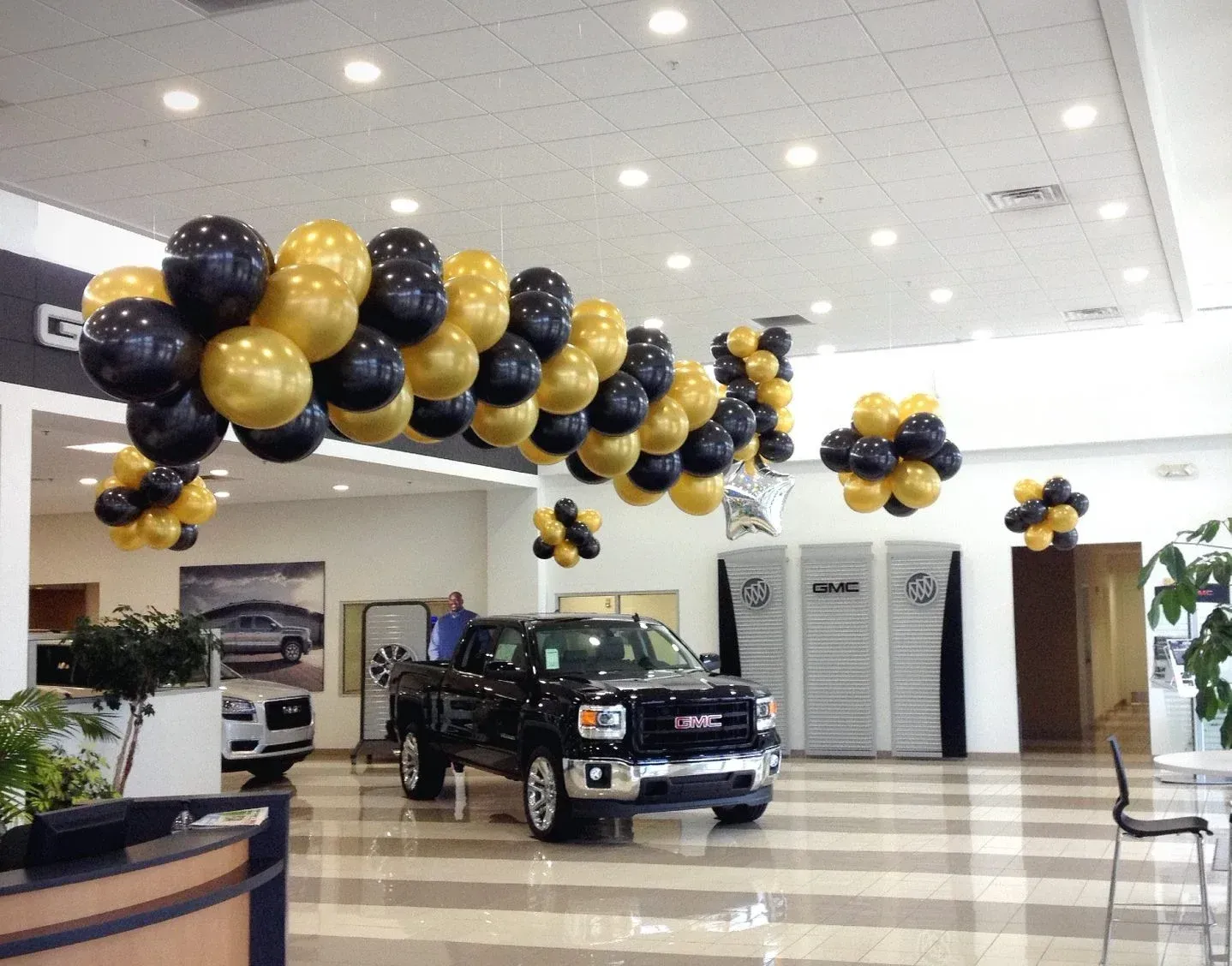 A gmc truck is parked in a showroom with balloons hanging from the ceiling