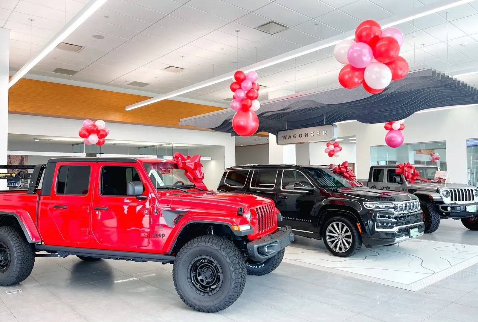 A jeep is parked in a showroom with balloons hanging from the ceiling.