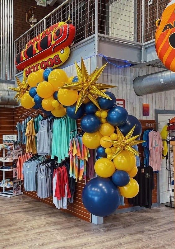 A store front decorated with yellow and blue balloons and a hot dog sign.