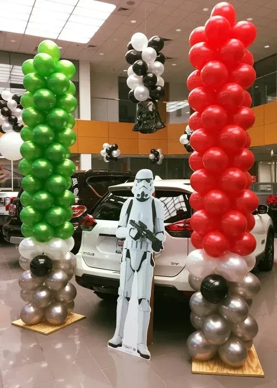 A storm trooper is standing in front of a car surrounded by balloons.