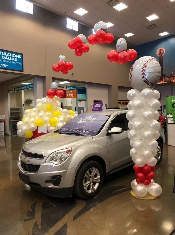A silver car is surrounded by balloons in a dealership