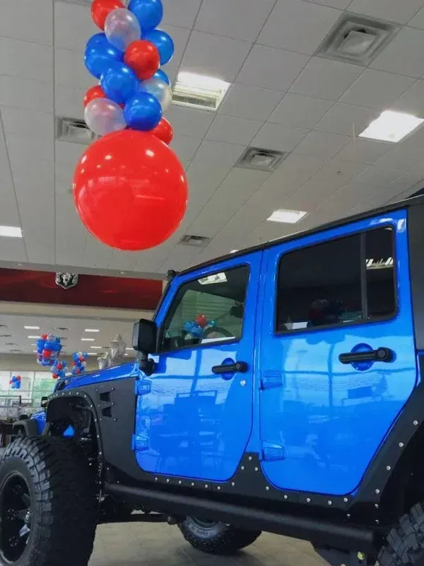A blue jeep with red white and blue balloons hanging from the ceiling