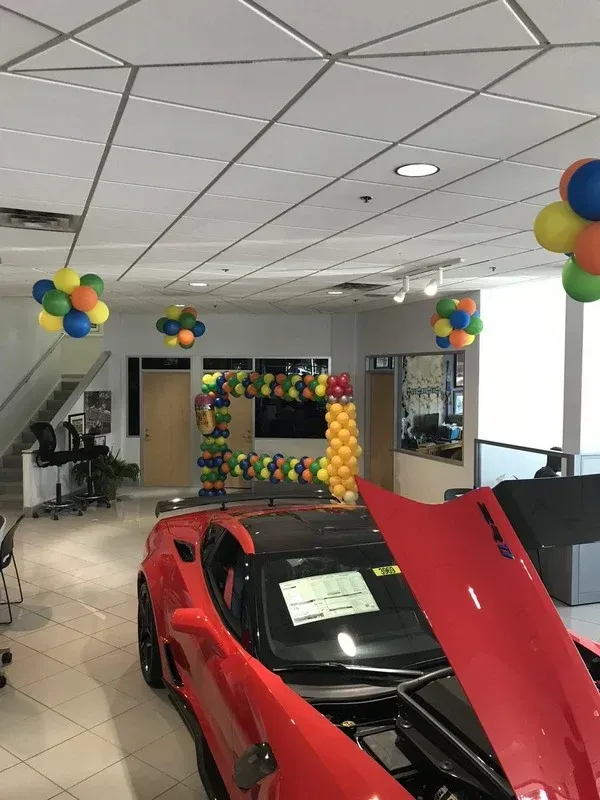 A red sports car with the hood open and balloons hanging from the ceiling