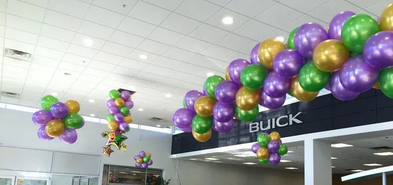 A bunch of balloons are hanging from the ceiling in a car dealership.