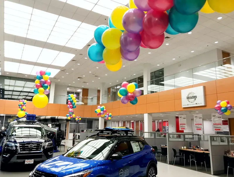 A blue car in a showroom with balloons hanging from the ceiling