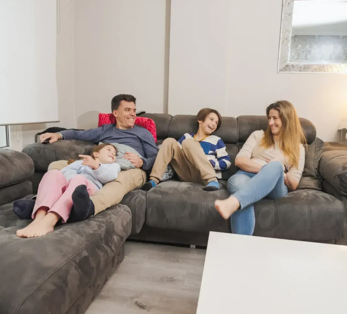 A family sits on a gray sectional sofa in a living room, talking and laughing together.