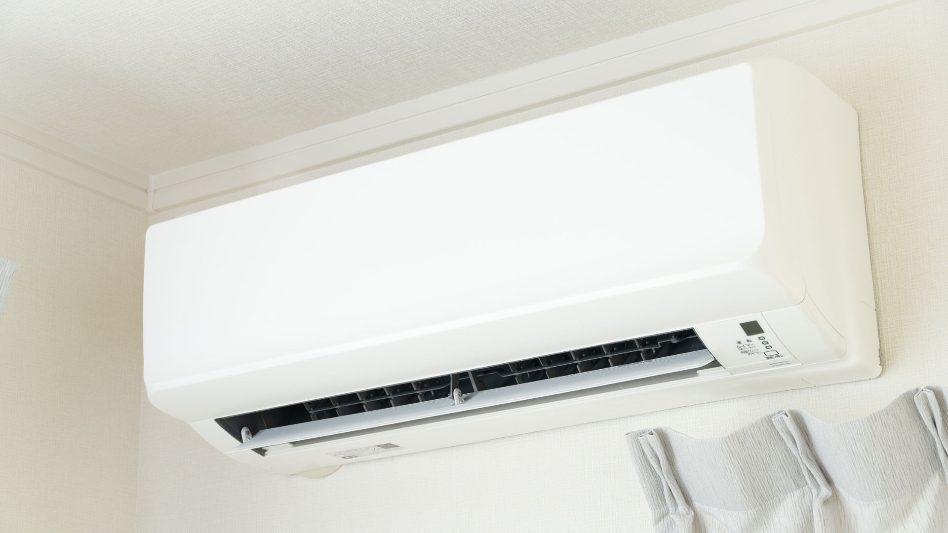 A white wall-mounted air conditioner unit installed near the corner of a room ceiling.