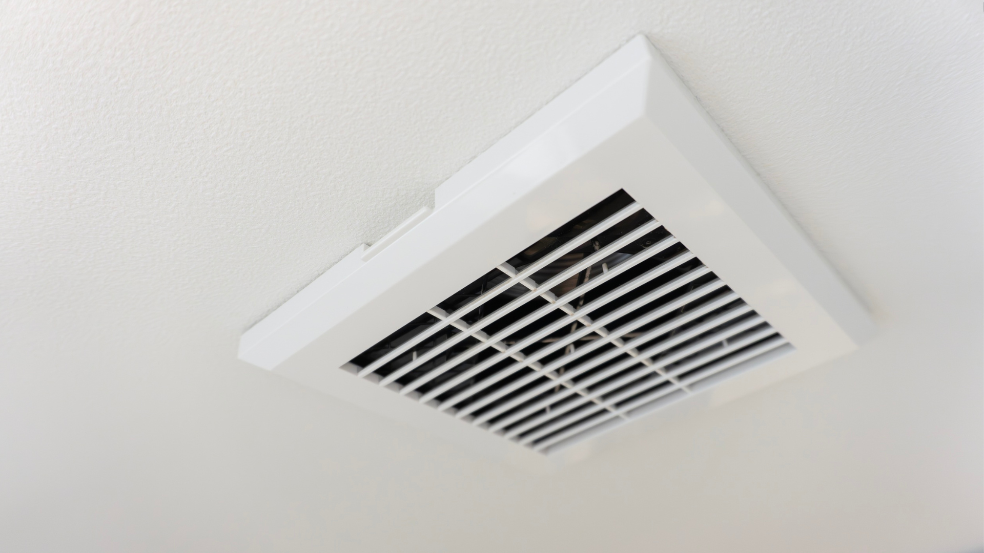 A white square ventilation fan installed on a matching textured ceiling.