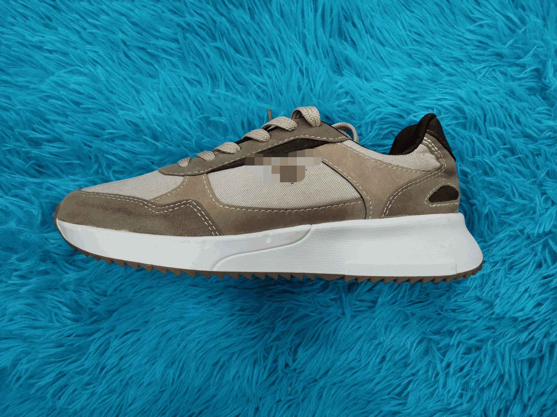 Zapatilla de color tostado y gris con suela blanca sobre una superficie esponjosa de color azul.