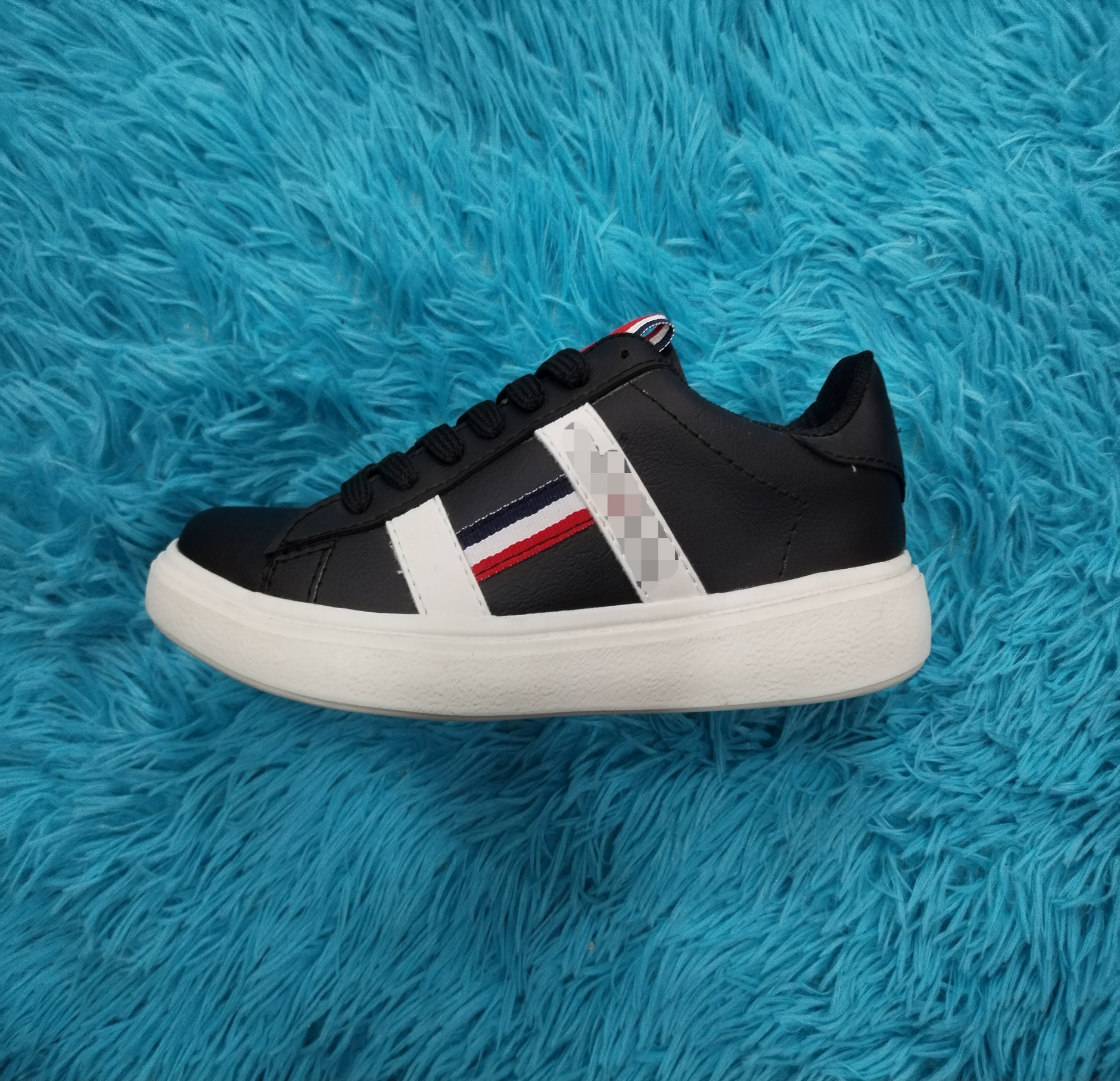 Zapatilla en color blanco y negro con detalles en rojo y azul, sobre una superficie difusa de color azul.