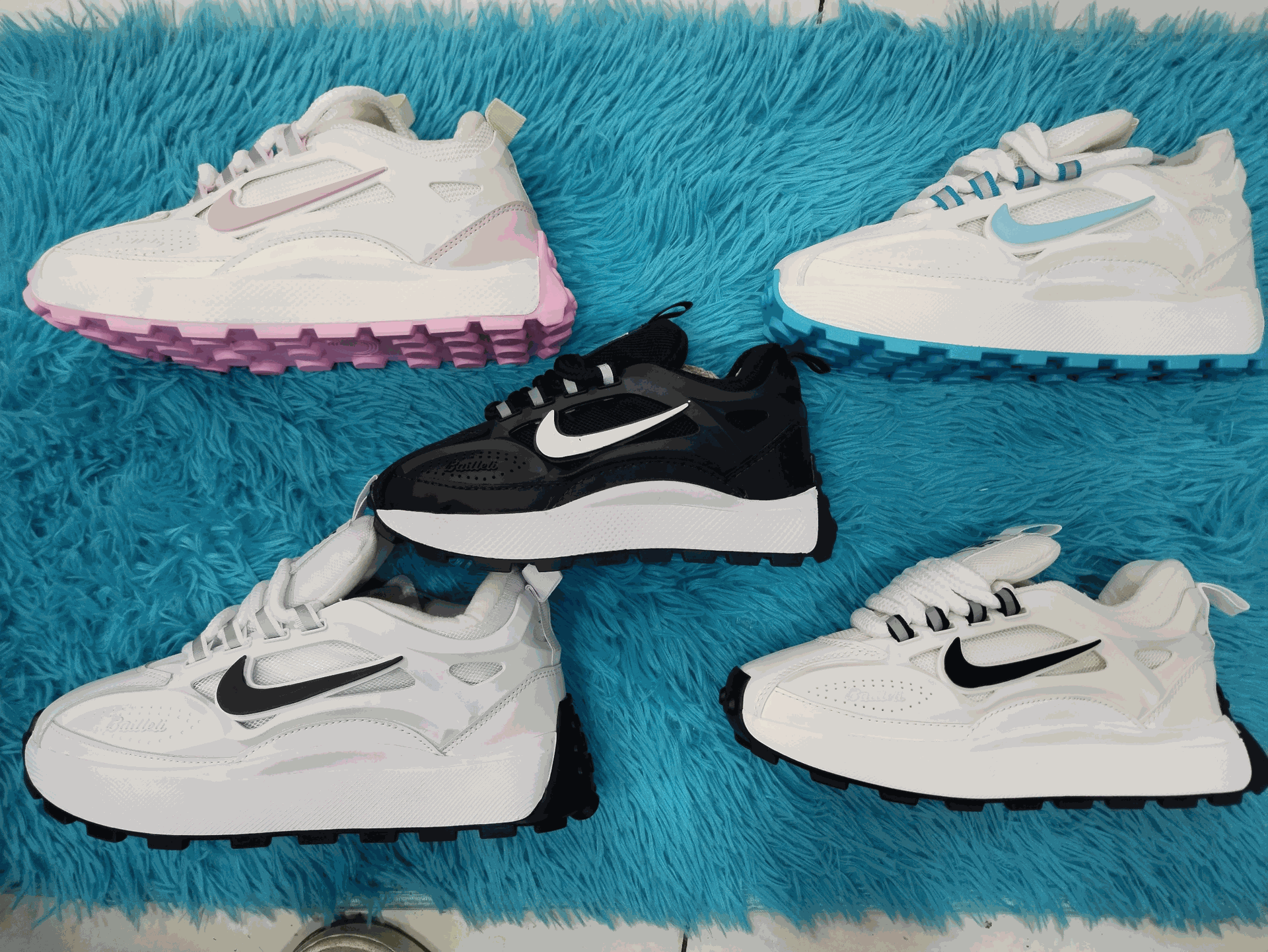 Cinco zapatillas blancas con detalles coloridos, dispuestas sobre una alfombra azul esponjosa.