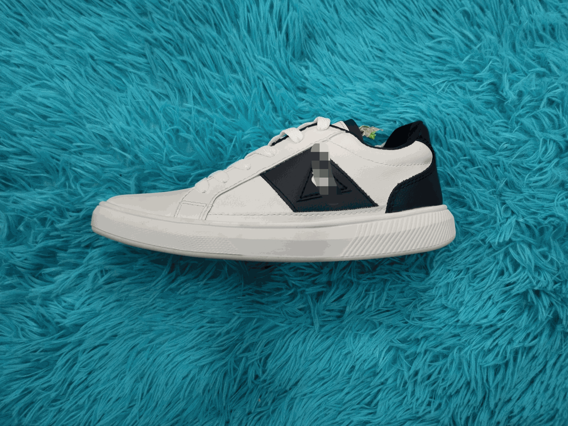 Zapatilla blanca y azul marino sobre una superficie esponjosa de color turquesa.