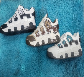 Tres zapatillas de bebé en blanco, marrón y azul sobre una alfombra peluda de color turquesa.