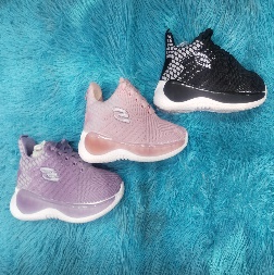 Tres pares de zapatillas de deporte para niños: negras, rosas y violetas, sobre una superficie azul esponjosa.