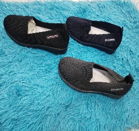 Tres zapatos negros sin cordones sobre una alfombra de pelo largo verde azulado. Dos zapatos están cerca uno del otro, el tercero está separado.