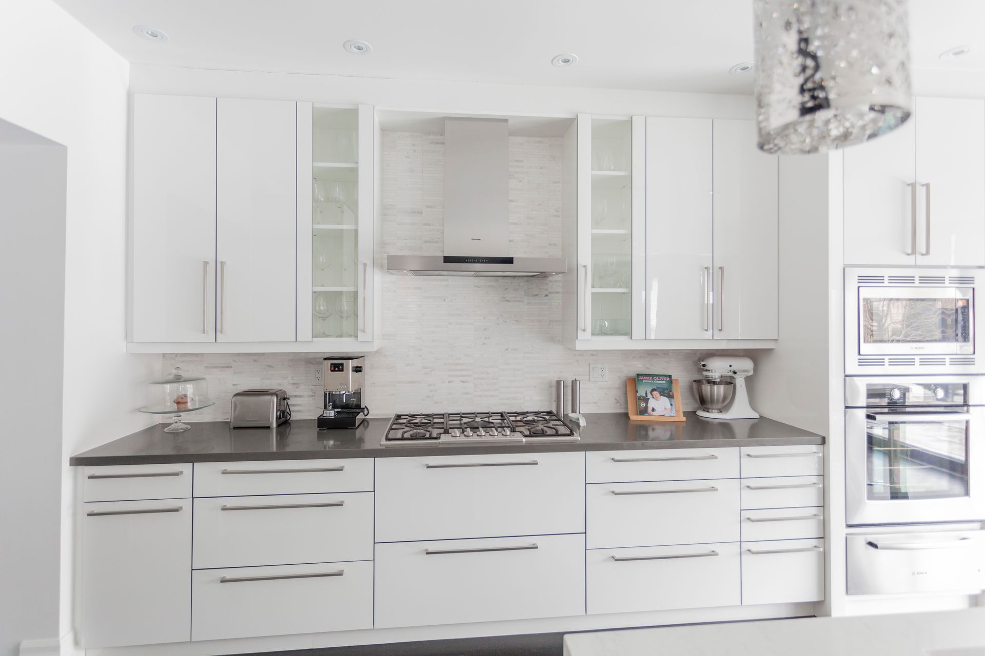 Contemporary kitchen with white cabinets, glass display cupboards, set against a white backsplash