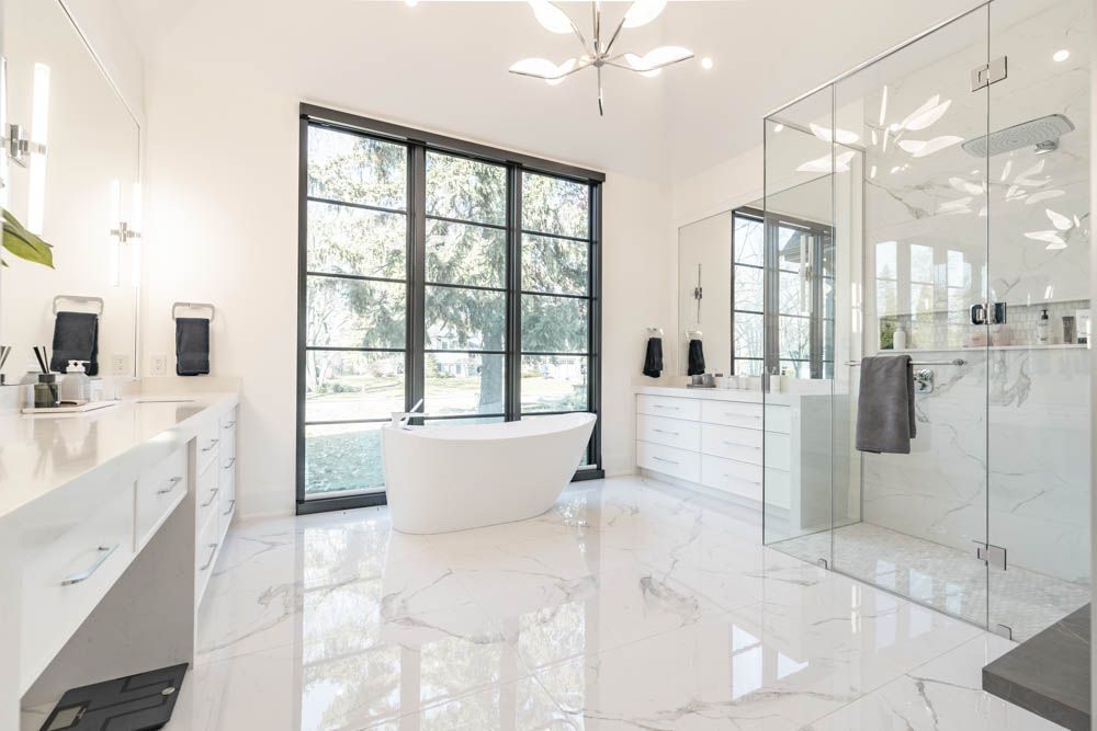 A bathroom renovation with free standing tub custom shower with custom double vanity cabinets design and a large mirrors on opposite walls
