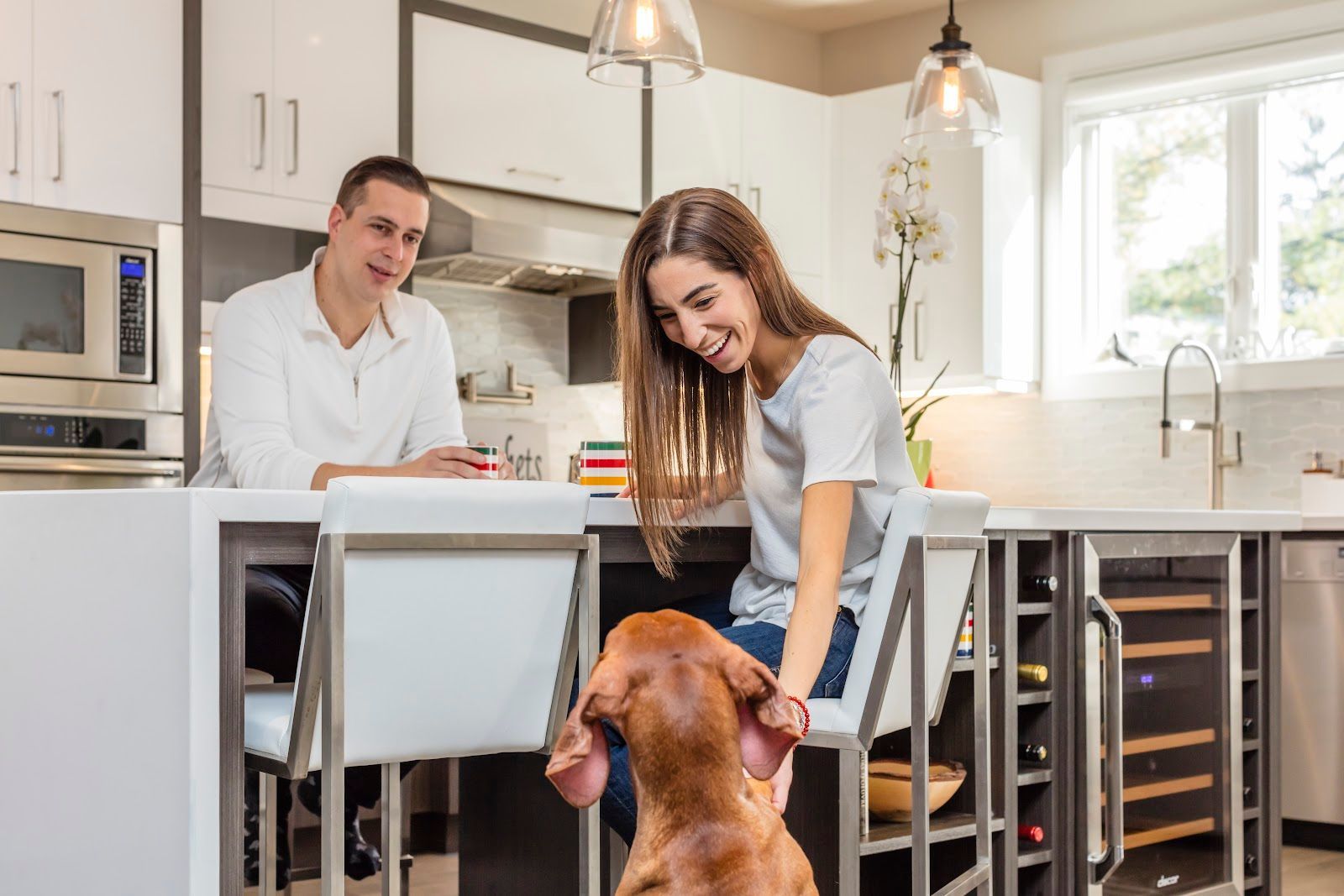 A man and a woman are sitting at a kitchen counter with a dog.