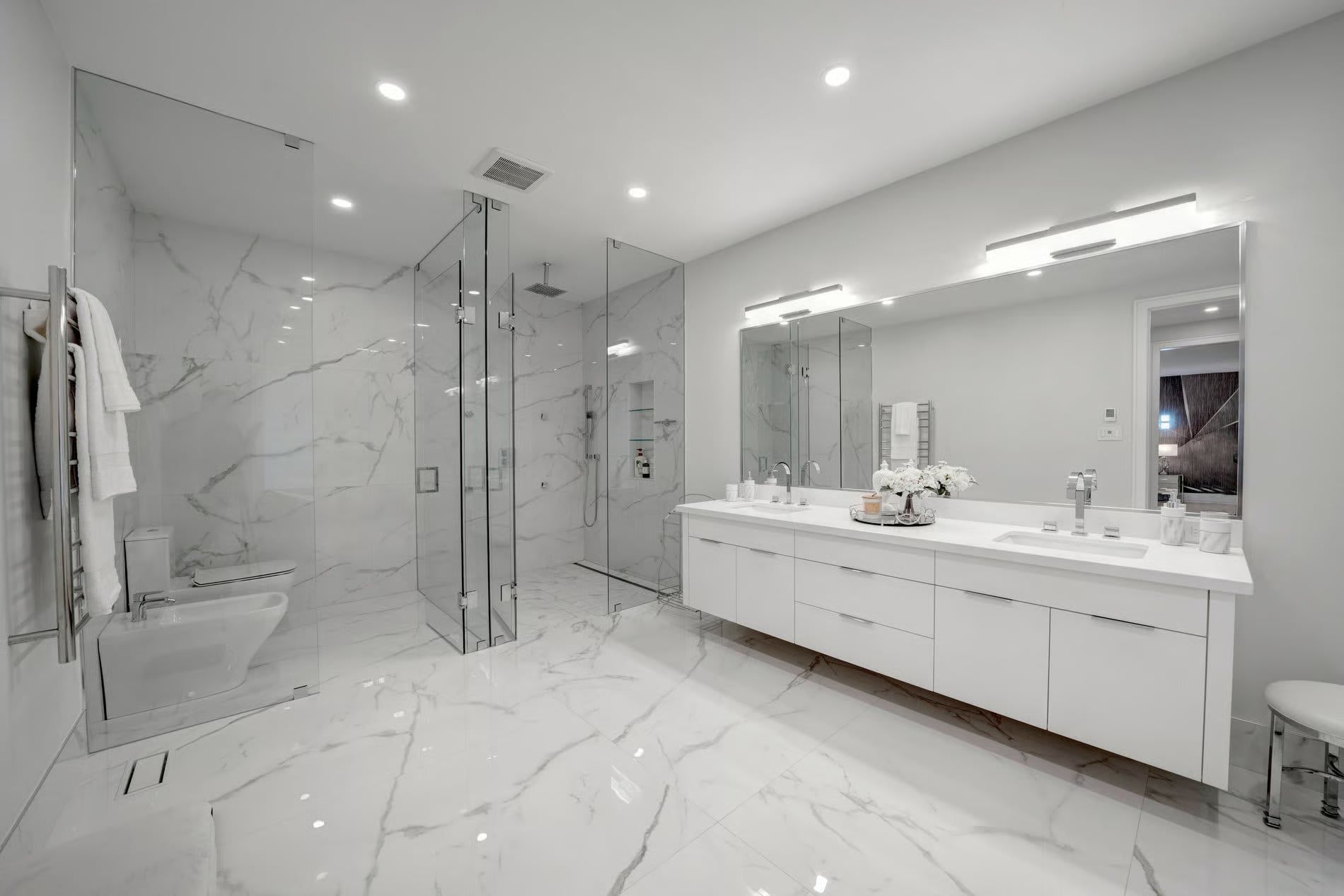 A bathroom renovation in Oakville by Kitchen Land designed with custom vanity cabinets with double sinks, tiled with marble tiles all throughout, with  a custom mirror and a walk in shower.