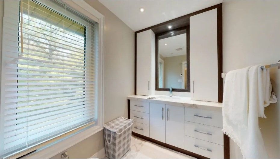A bathroom with a sink , mirror , cabinets and a window.