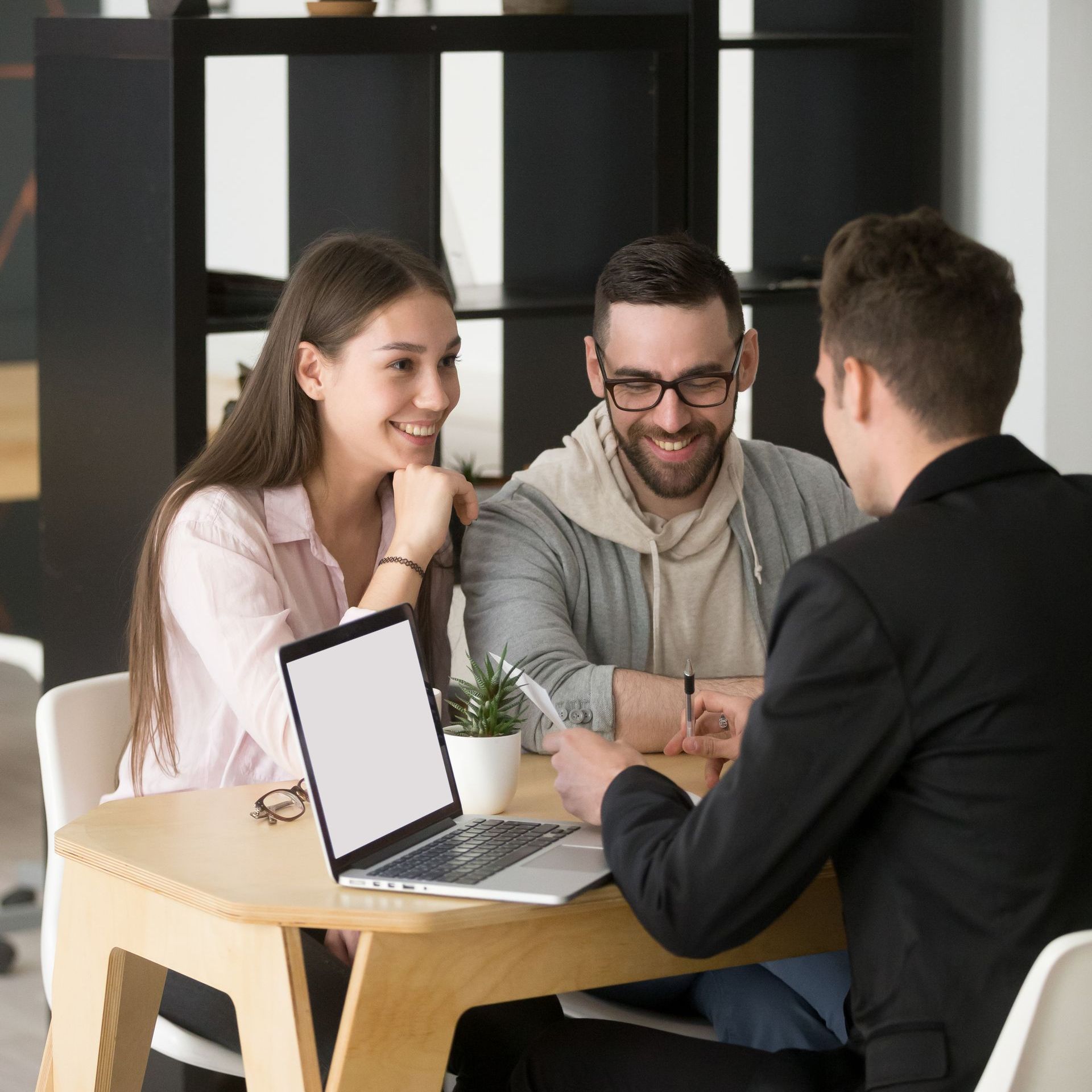 A group of people are sitting around a table with a laptop on it.