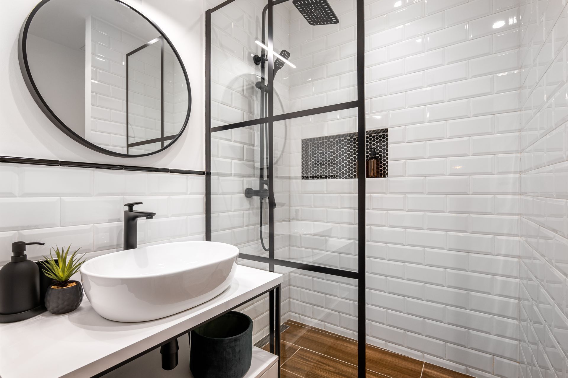 A bathroom with white tiles , a sink , a mirror and a walk in shower.